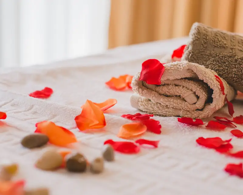 Soft towels rolled up on a bed scattered with colorful rose petals and smooth stones, creating a serene and inviting spa atmosphere.